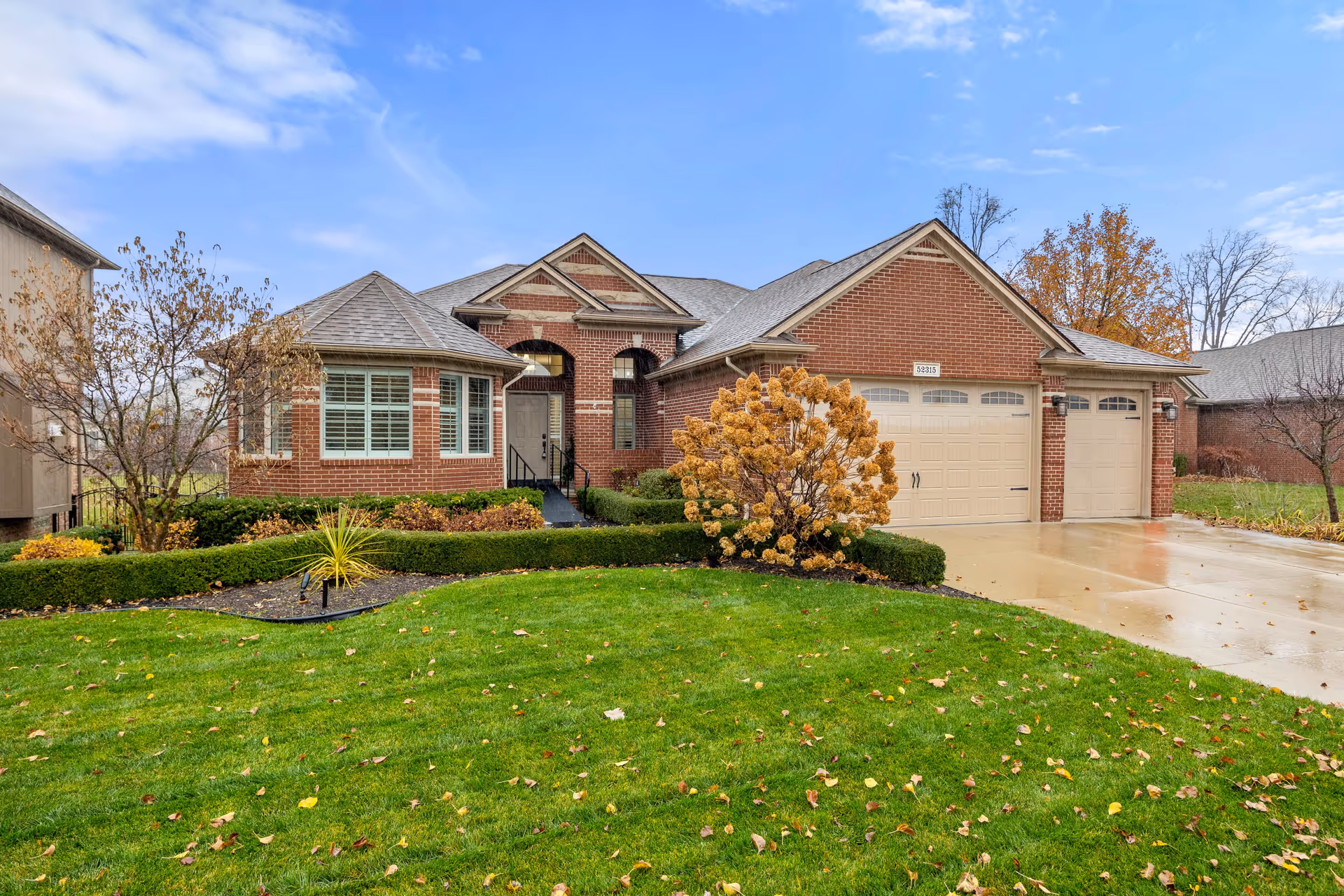 Brick ranch-style house with an attached two-car garage, manicured front lawn and shrubs under a blue sky.