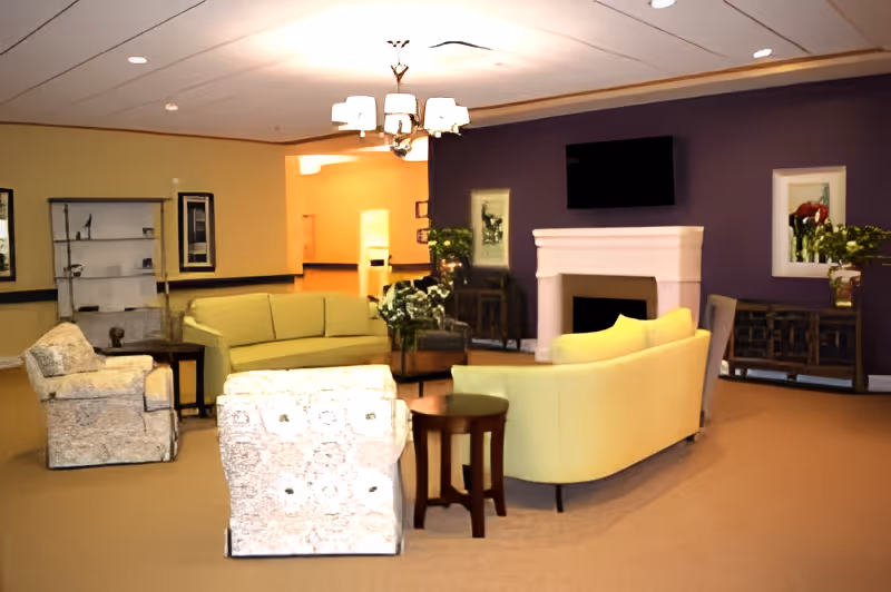 Communal lounge with sofas and armchairs arranged around a fireplace and wall-mounted TV.