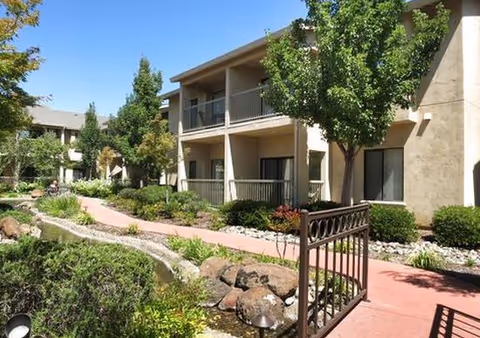 Exterior view of a two-story senior living building with balconies and landscaped walkways.