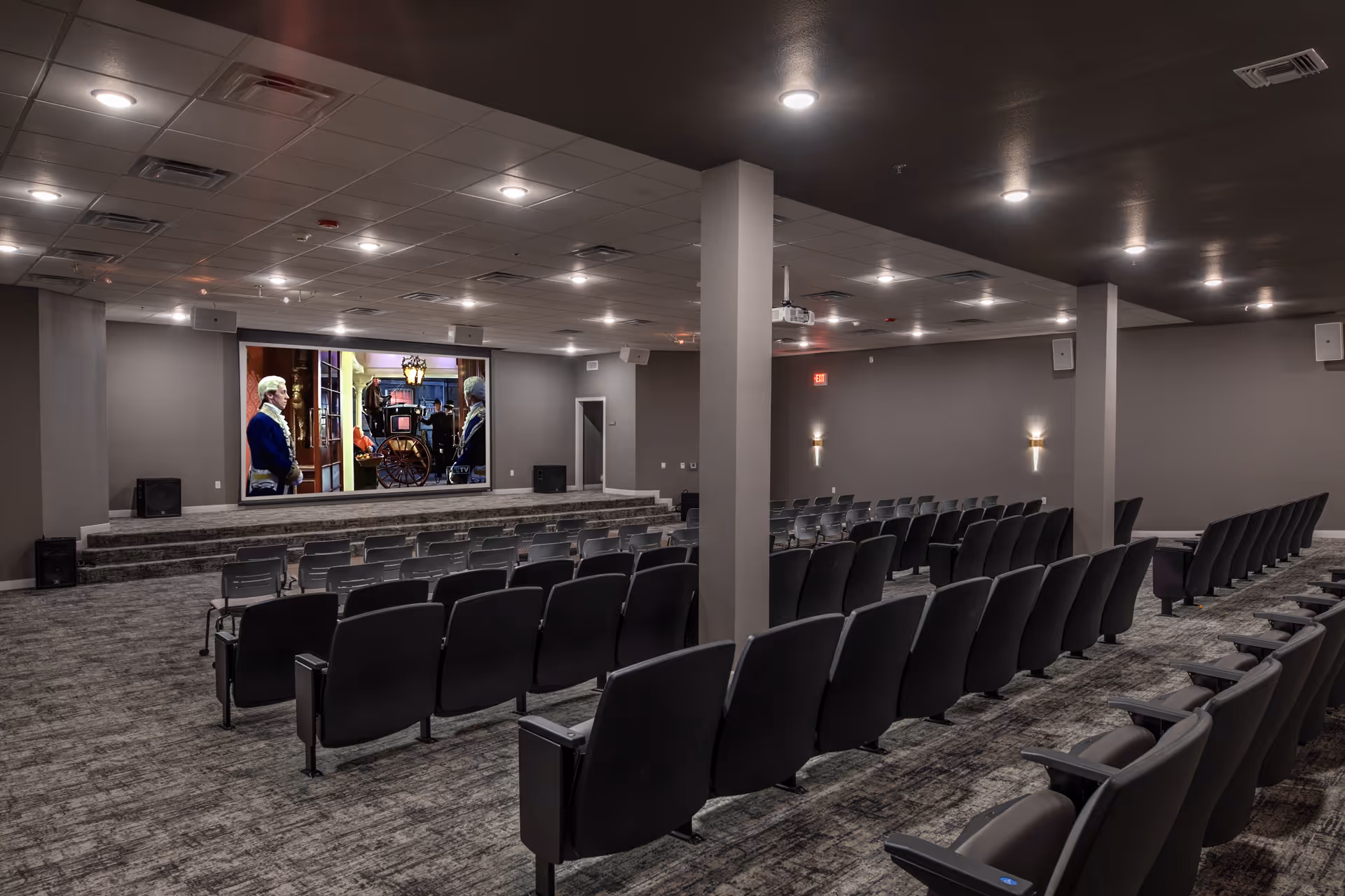 Large auditorium-style theater room with rows of reclining seats facing a stage and a projection screen.