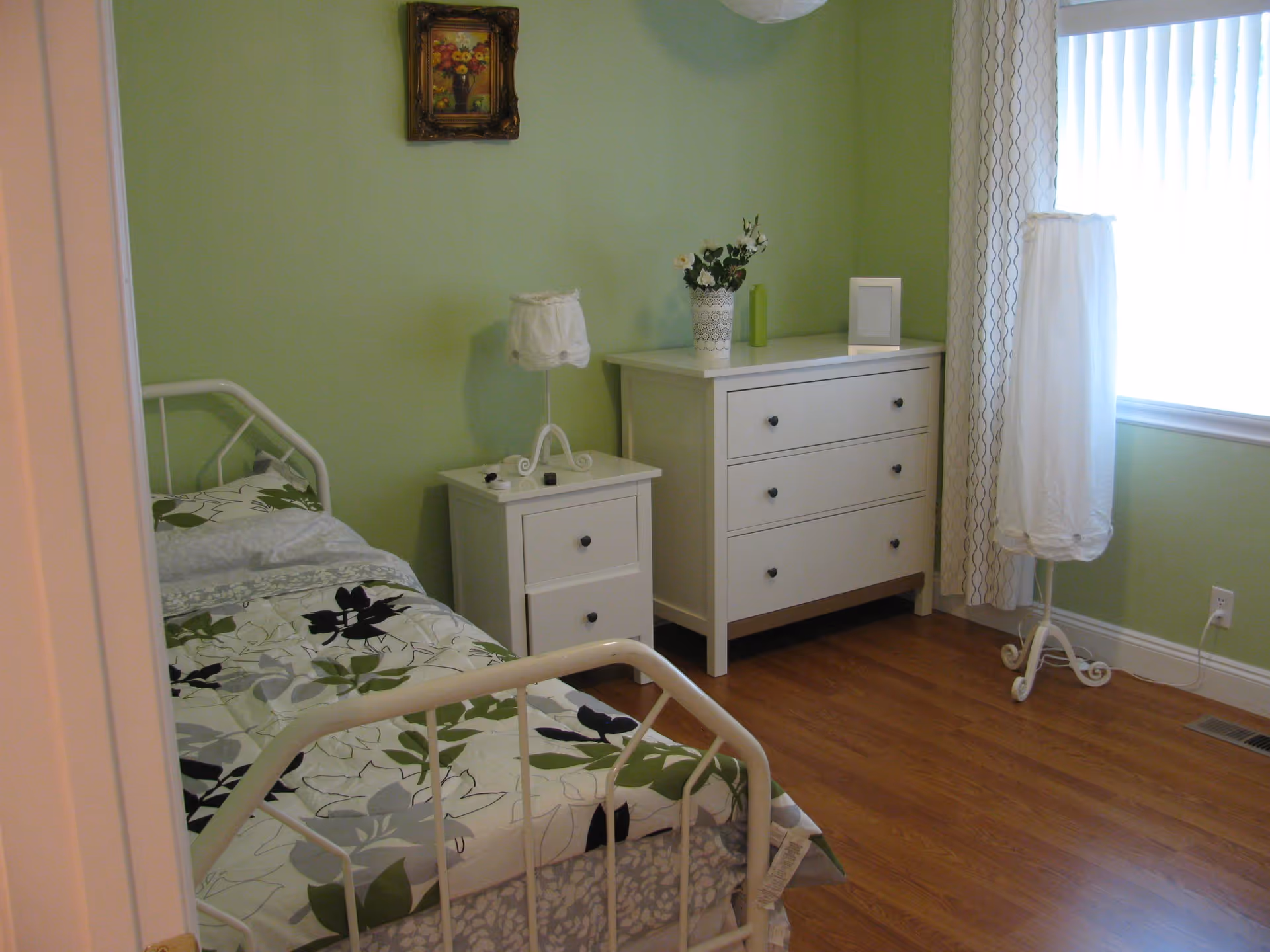 Cozy bedroom with a white metal bed, matching white dresser and nightstand, green walls, and hardwood floor.