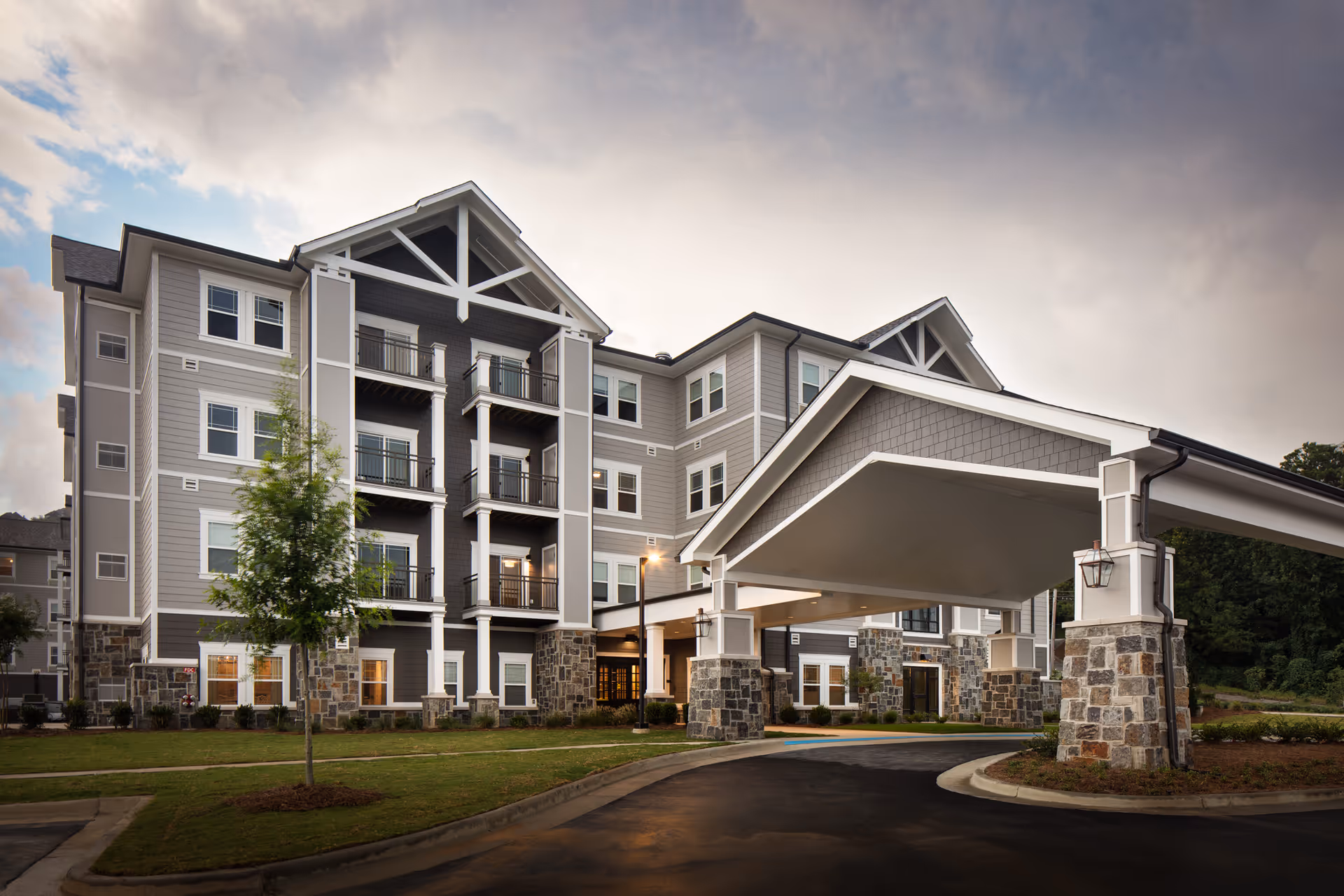 Exterior view of Monark Grove Greystone senior living building with a porte-cochere and stone accents.