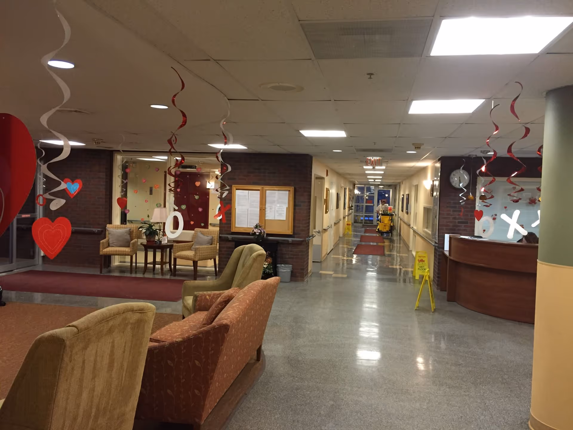 Interior lobby of a senior living facility with seating, a reception desk and a long decorated corridor.
