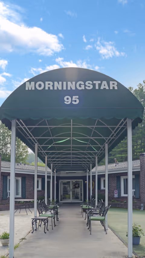 A curved green canopy with 'MORNINGSTAR 95' over a covered walkway leading to the facility entrance, with black metal chairs along both sides.