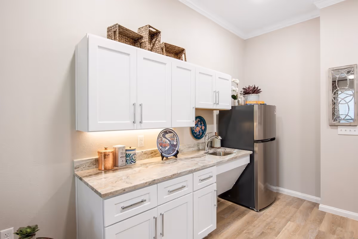 Small kitchen area with white cabinets, marble countertop, sink, and a stainless steel mini refrigerator.