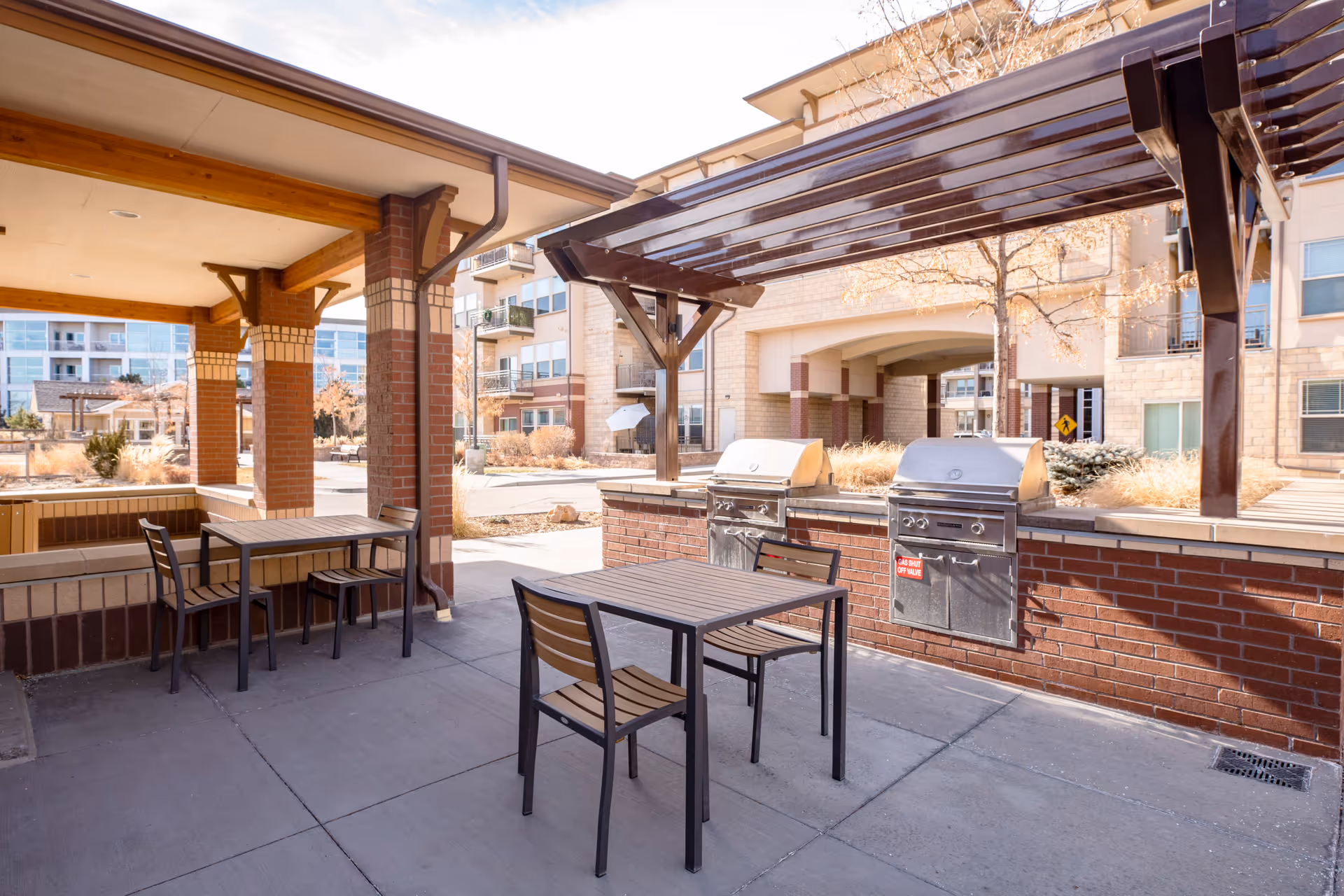 Outdoor courtyard with covered seating, tables and built-in stainless steel grills in front of a multi-story apartment building.