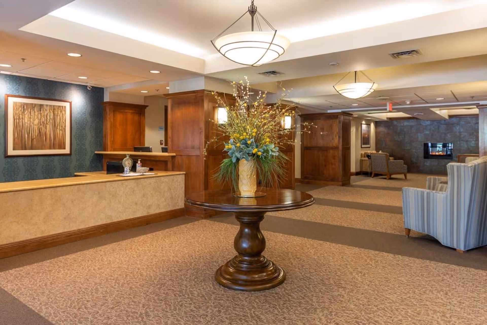 Bright, furnished lobby with a round pedestal table topped with a large floral arrangement, reception desk, and seating areas.