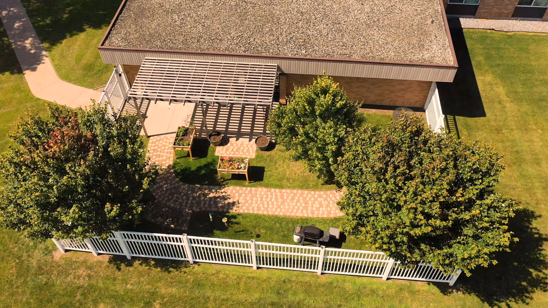 Aerial view of a fenced courtyard with a pergola, paved walkway, planter boxes and trees next to a building.