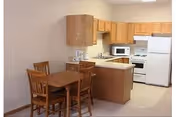 Small kitchenette with wooden cabinets, white appliances, and a wooden dining table with four chairs.