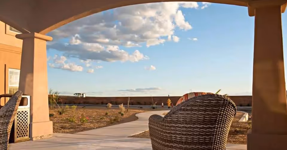 Covered patio with wicker chairs overlooking a landscaped walkway and open sky.