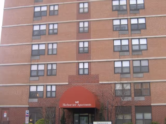 A multi-story brick apartment building with a red arched entrance canopy reading Harborview Apartments.