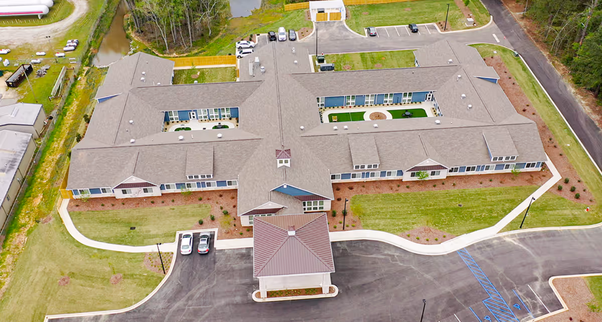 Aerial view of The Colonial at Old Camden senior living facility showing a large, single-story building with multiple wings, surrounded by parking areas, green lawns, and pathways.