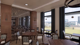 Interior view of a dining area with wooden tables and chairs. Large windows provide a view of a green outdoor space and city buildings in the distance. The room features a decorative wall with a geometric pattern and recessed lighting in the ceiling.