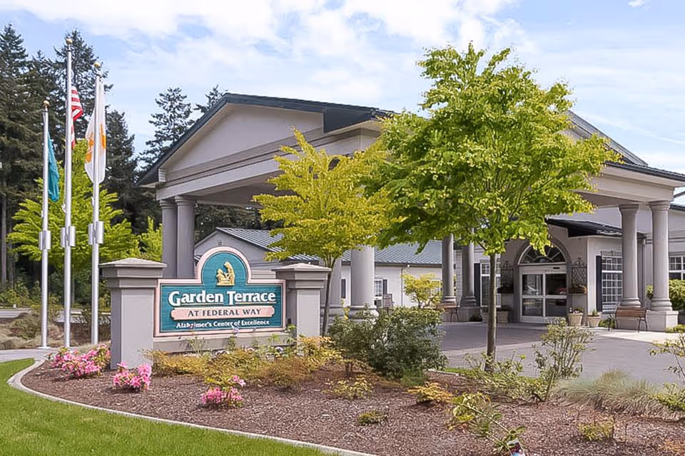 Front entrance of the Garden Terrace senior living facility with a driveway, entry columns, landscaped beds and a prominent sign.