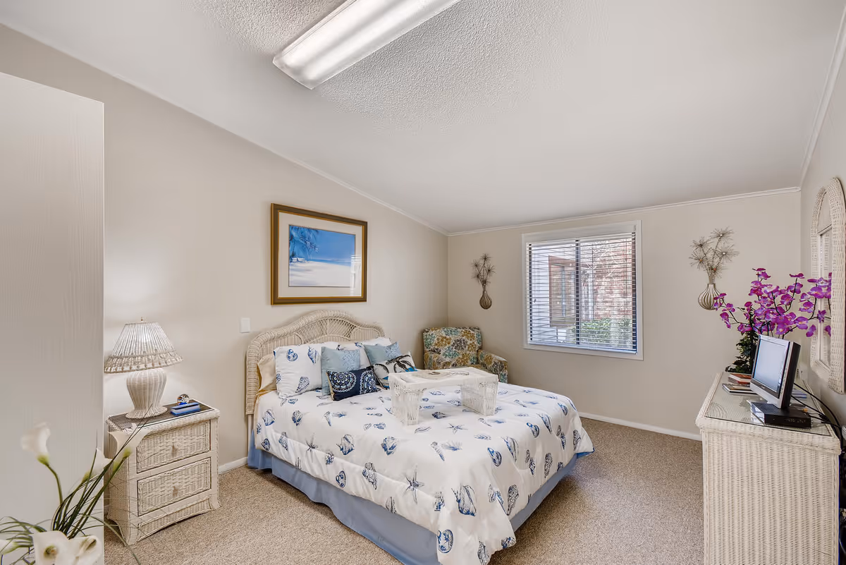 Cozy bedroom featuring a bed with sea-themed bedding, wicker nightstand and dresser, window, armchair, and decorative accents.