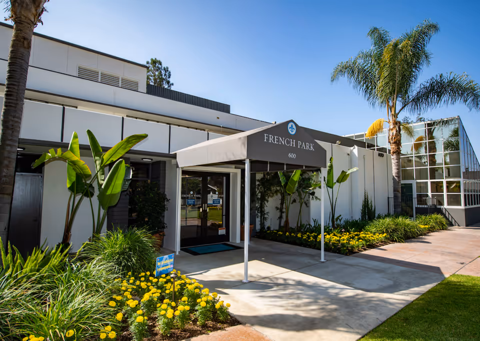 Front entrance of French Park Care Center with a covered awning, glass doors, and landscaped flowerbeds.