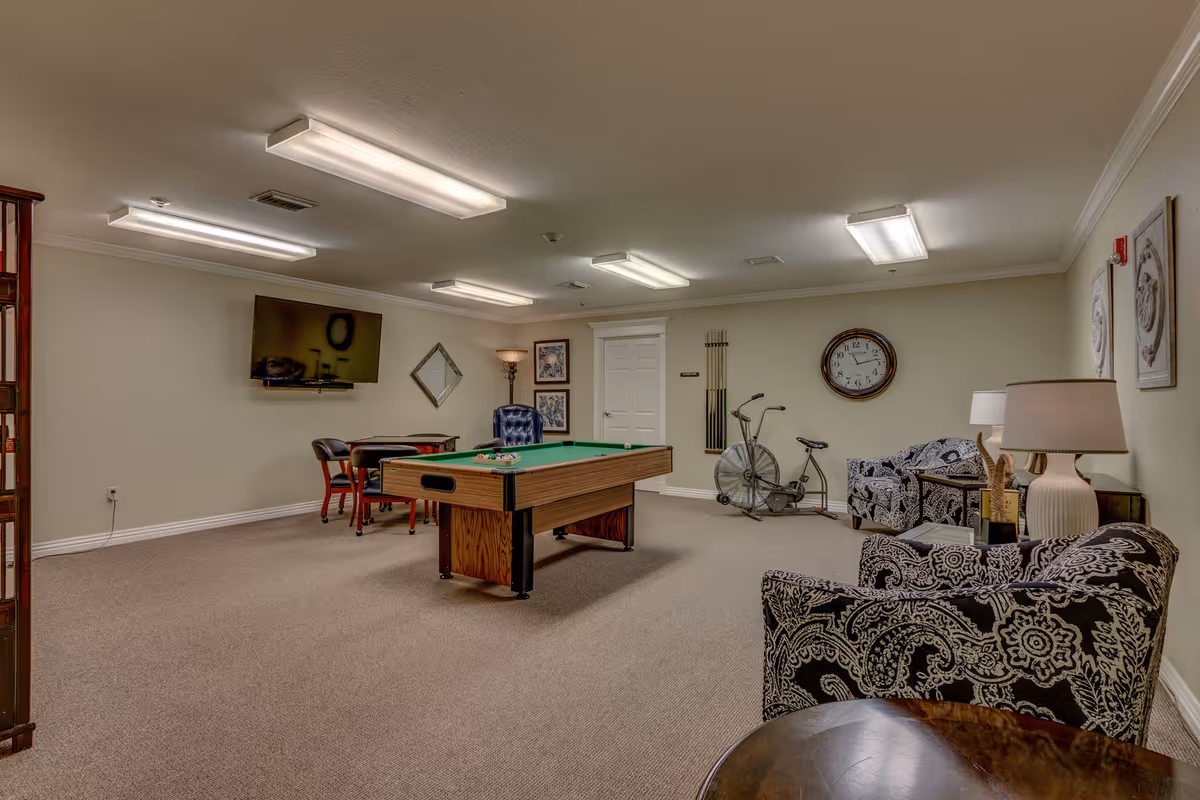 Recreation room with a pool table, seating area, wall-mounted TV, and an exercise bike.