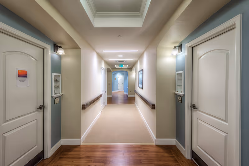 Well-lit interior corridor with doors on both sides, handrails, and recessed ceiling lighting.