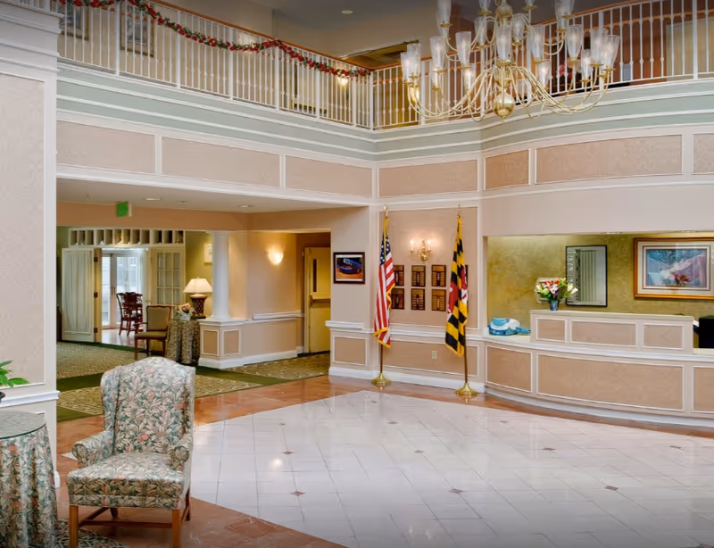 Bright two-story lobby with chandelier, reception desk, seating area, and flags.