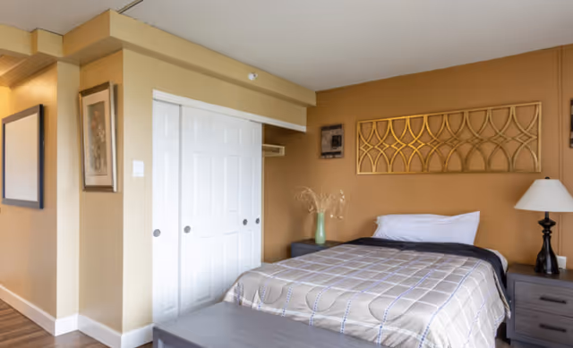A furnished bedroom with a bed, nightstands, a lamp, decorative wall art, and a closet with white sliding doors.