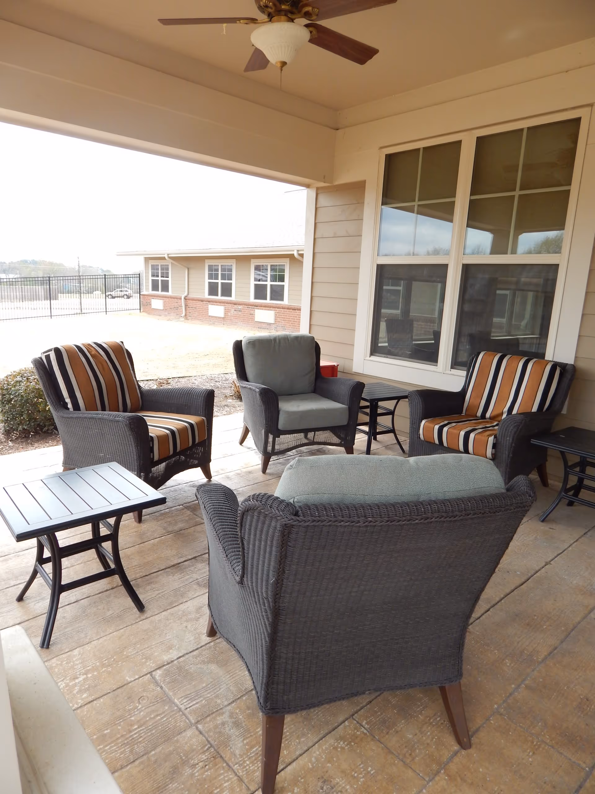 Covered outdoor patio with wicker chairs, striped cushions, small tables and a ceiling fan outside the facility.