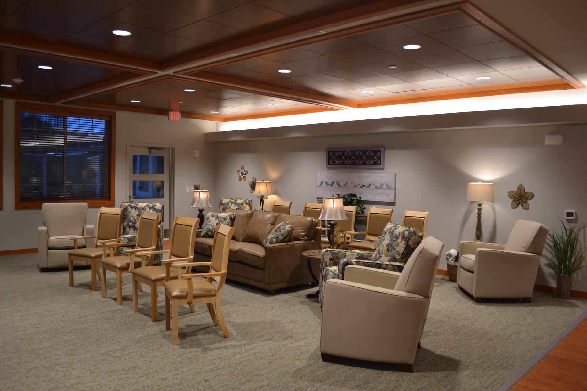Spacious communal lounge with sofas, armchairs, lamps and arranged seating in a senior living facility.