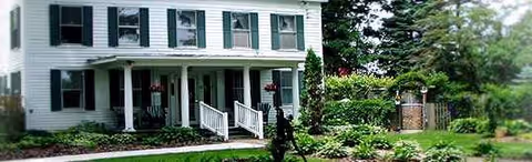 Two-story white building with green shutters and a front porch, landscaped surroundings.