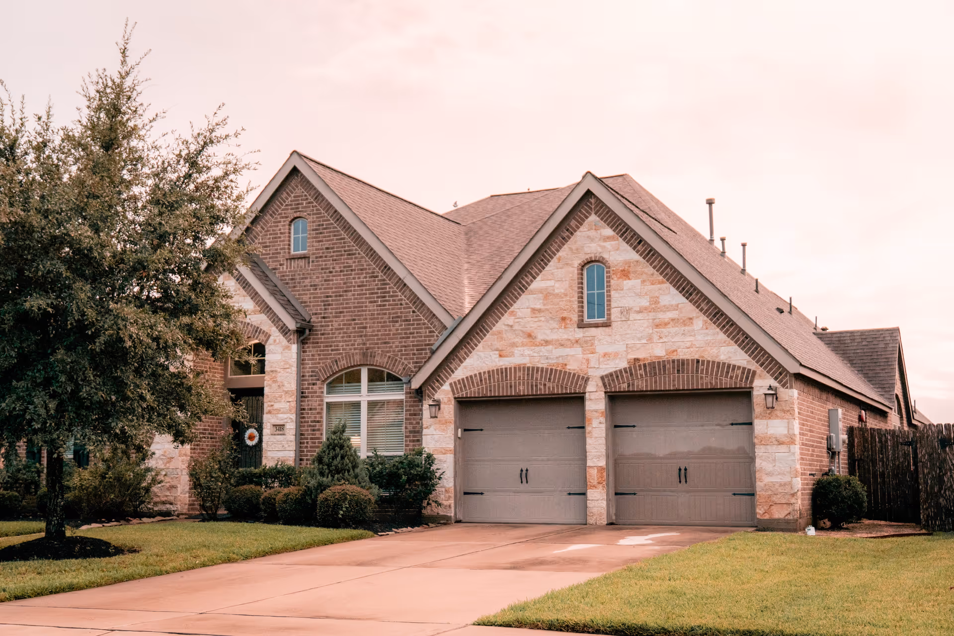 Brick and stone suburban house with a two-car garage, driveway, and landscaped front yard.
