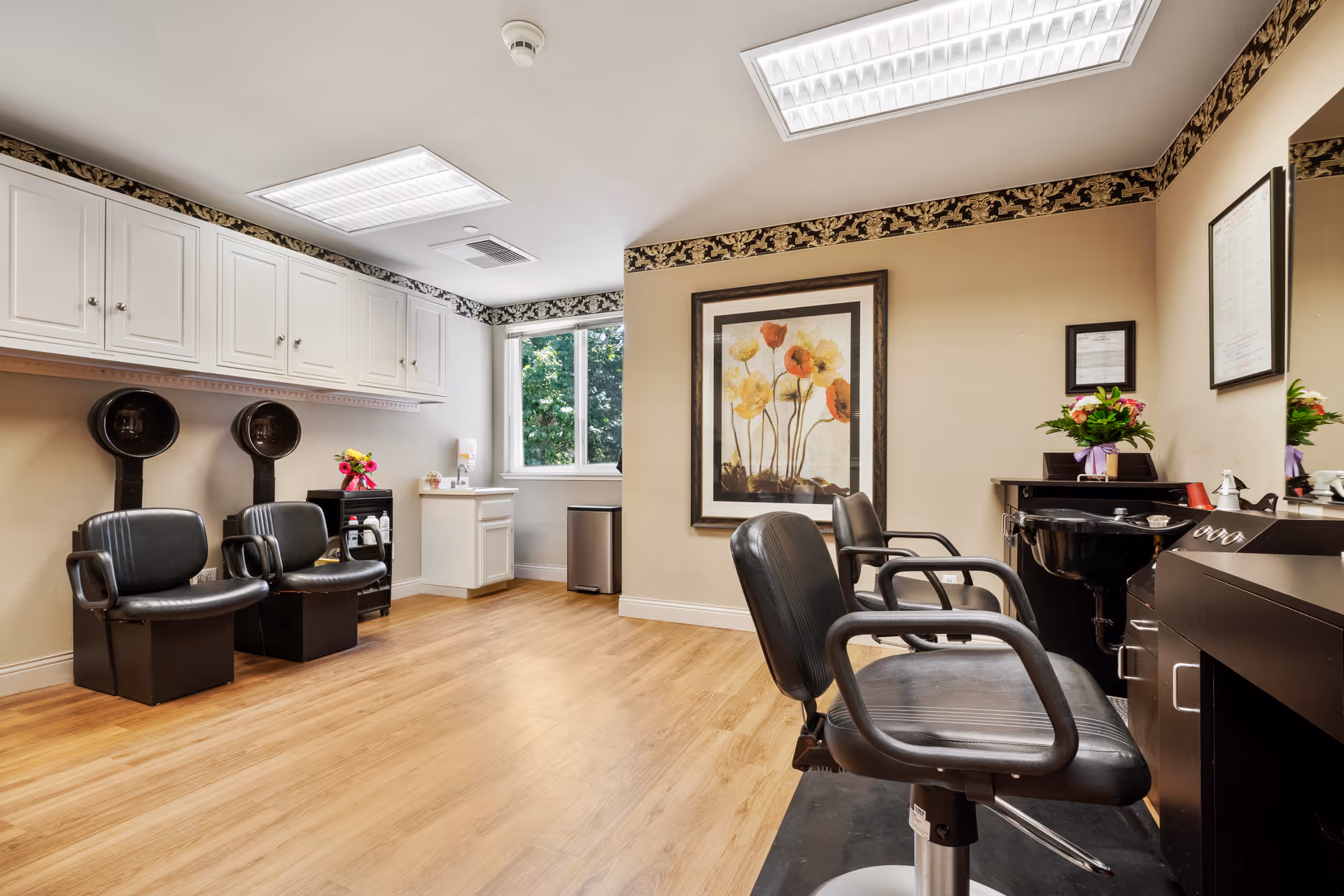Interior salon with styling chairs, shampoo stations, white cabinetry, wood floor and a large floral wall art.