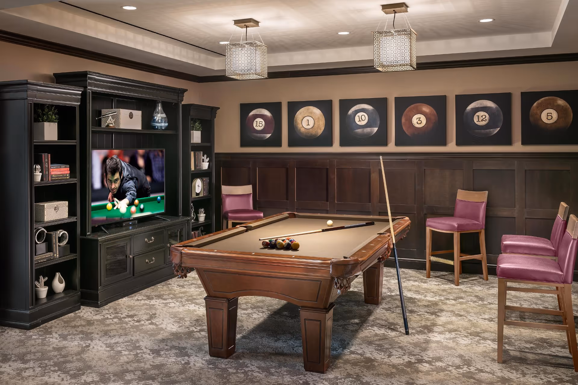 A billiards room with a pool table, cue sticks, purple chairs, a TV in a dark wood entertainment unit, and framed billiard ball artwork on the wall.