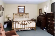 A furnished bedroom with an ornate metal bed, dressers, nightstands, and a TV.