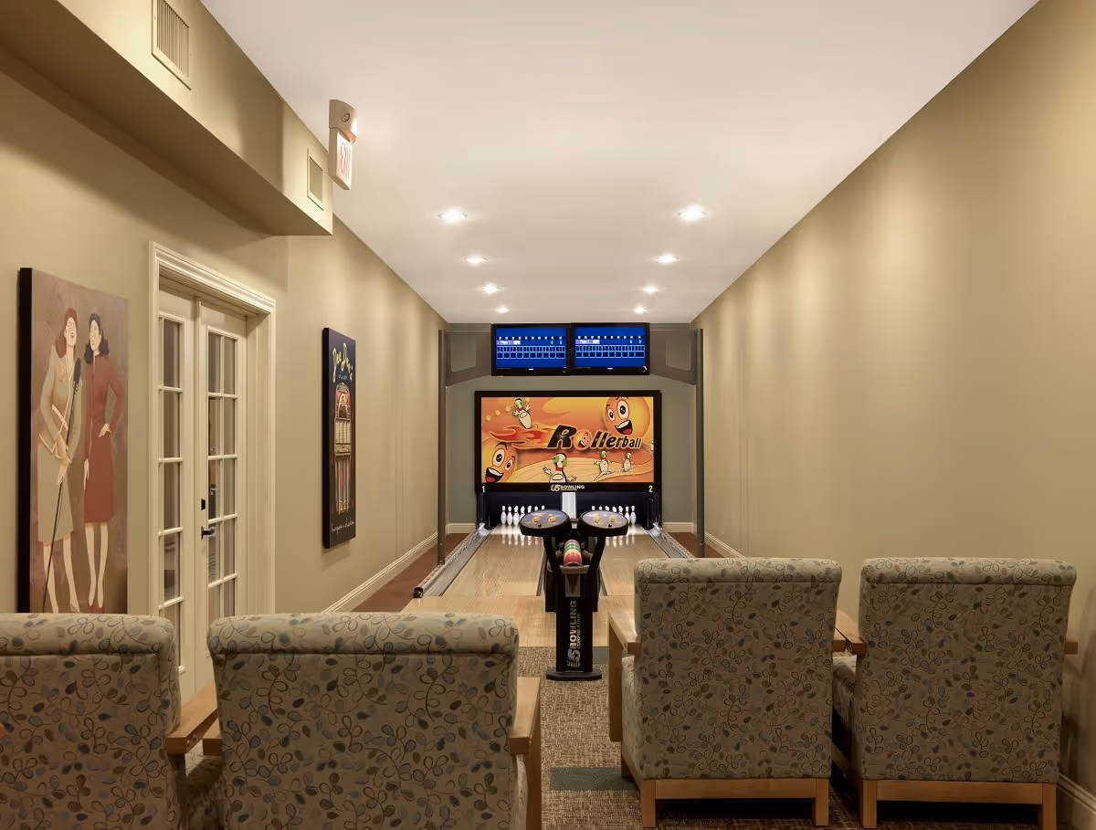 Small indoor bowling lane with four upholstered chairs facing the pins and colorful wall art.