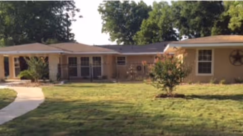Single-story ranch-style building with a front lawn, curved walkway, and mature trees.