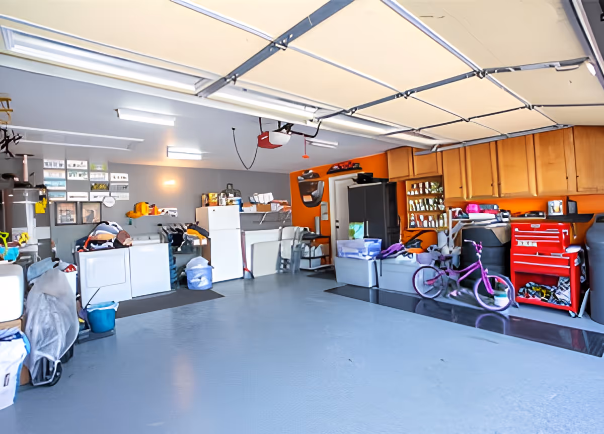 Spacious garage interior with storage cabinets, washer/dryer units, a red tool chest, and a pink bicycle.