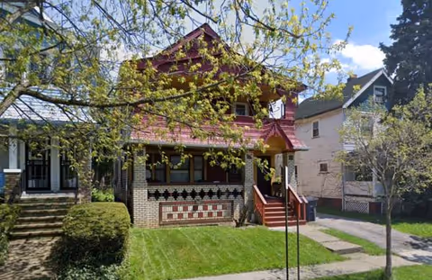 Front view of a brick house with red porch steps and a green lawn.