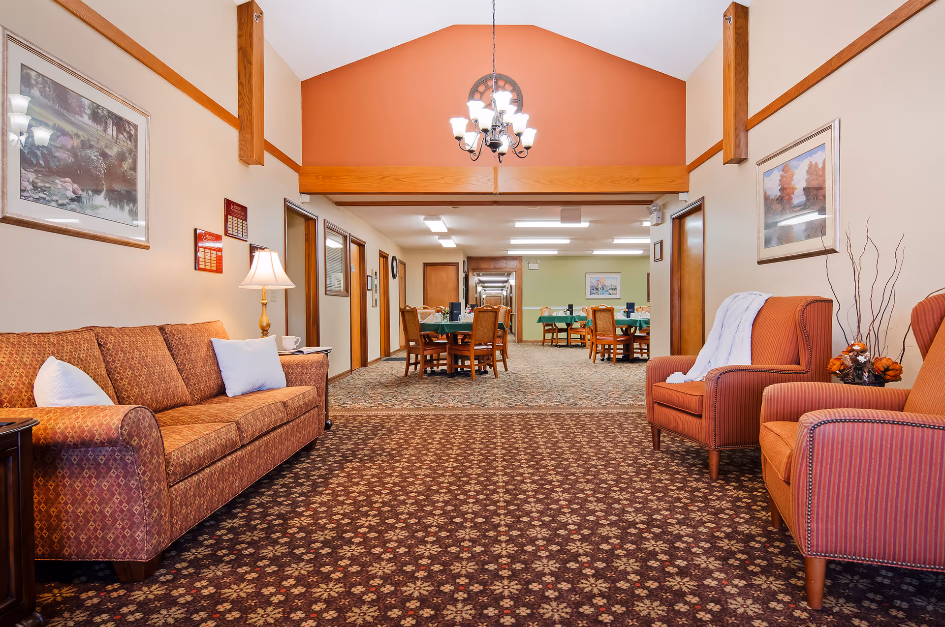 Cozy common room with patterned sofa and armchairs opening onto a dining area with tables and chairs.