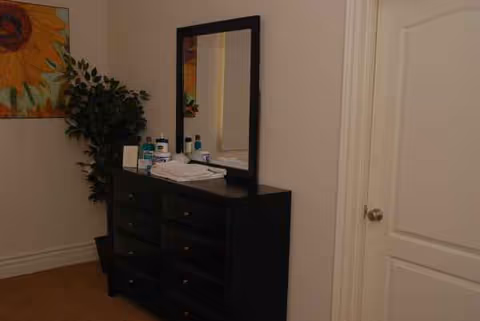 Dark dresser with a mirror in a hallway, bottles and towels on top.