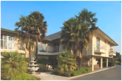 Two-story senior living building with exterior balconies, palm trees, and a fountain by the entrance under a clear blue sky.