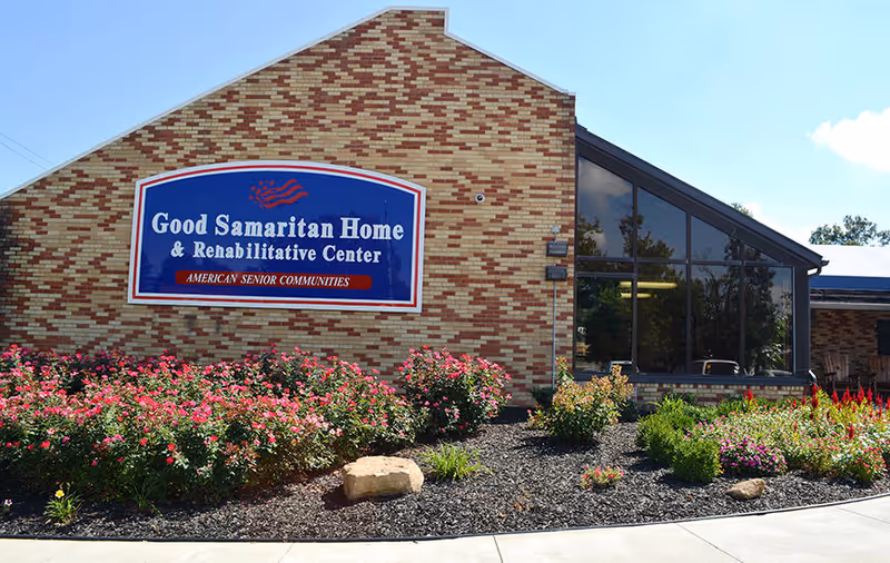 Brick building facade with a large "Good Samaritan Home & Rehabilitative Center" sign above landscaped flower beds.
