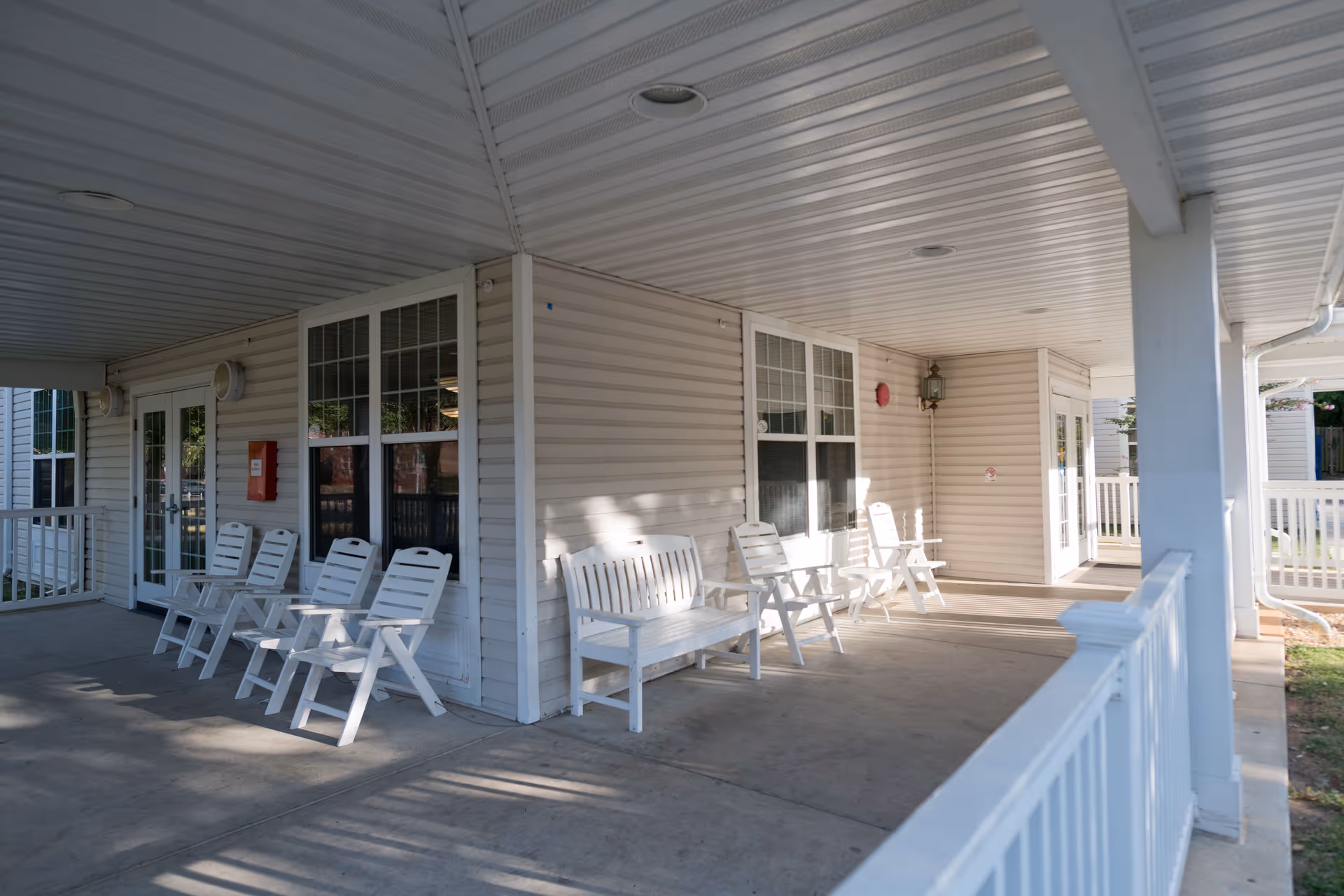 Covered exterior porch with white chairs and benches along the entrance of a senior living facility.