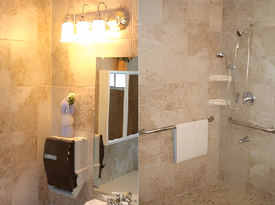 Tiled accessible bathroom with a walk-in shower, grab bars, vanity mirror, light fixture and wall-mounted dispensers.
