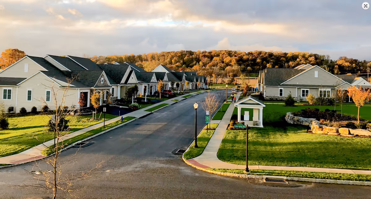 A view of the exterior of Homestead Village featuring several houses along a tree-lined street, with vibrant fall foliage in the background and well-maintained lawns.