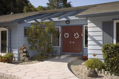 Front exterior of a blue building with double red doors and wreaths.