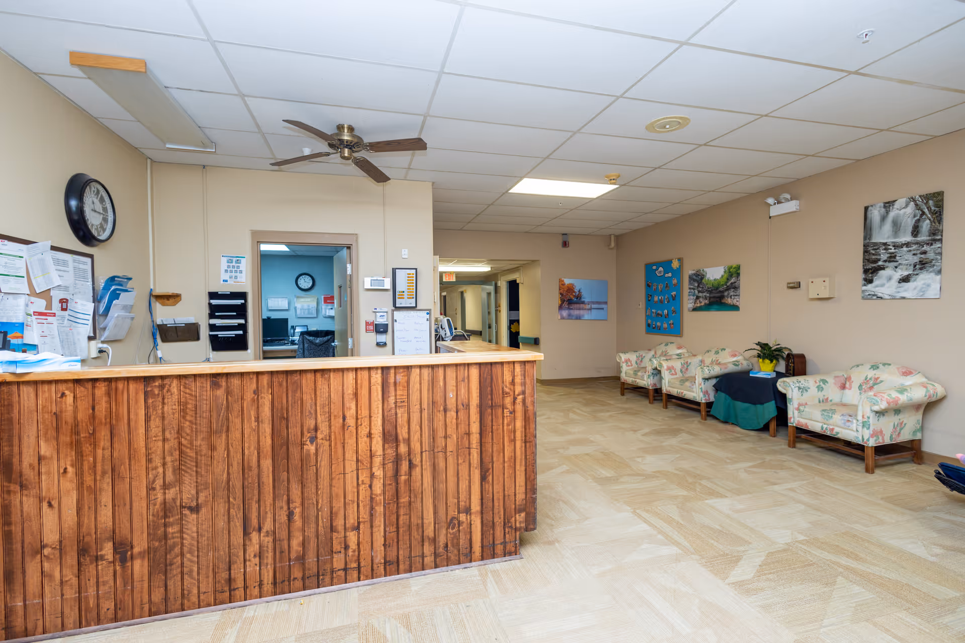 Reception desk and lobby area with a wooden front counter, floral upholstered chairs along the right wall, and a ceiling fan.