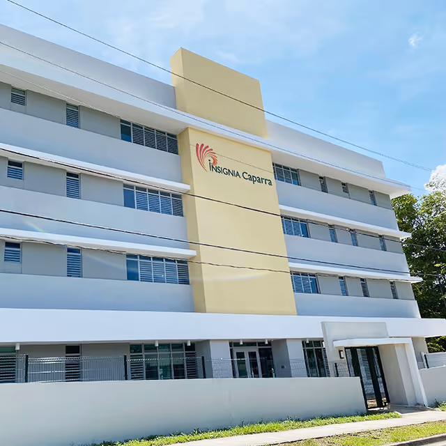 Front facade of the multi-story Insignia Caparra building with a pale yellow central section and rows of windows.
