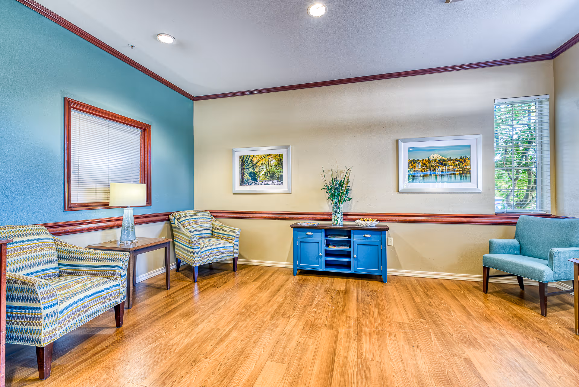 Bright seating area with patterned armchairs, a blue console table, framed artwork, and hardwood floors.