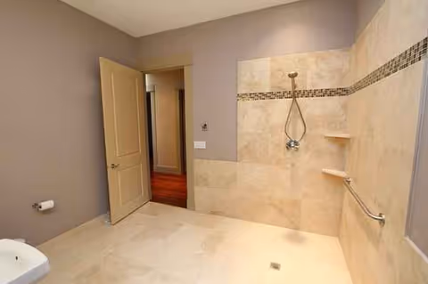 Beige tiled bathroom with a walk-in shower, grab bars, and a doorway to a hallway.