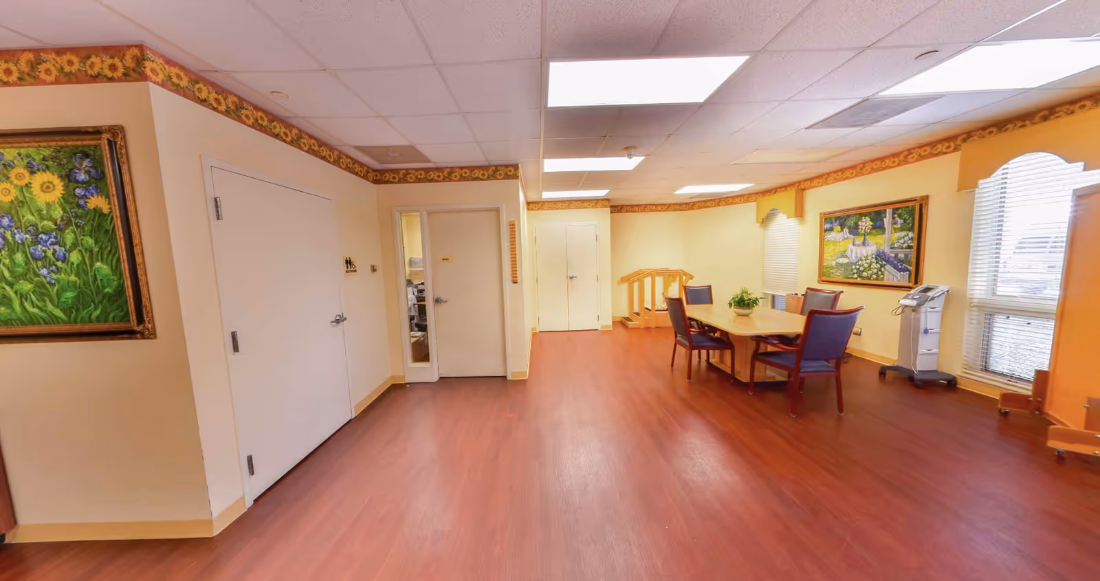 Spacious interior common/dining area with a table and chairs, artwork on the walls, and wood-look flooring.
