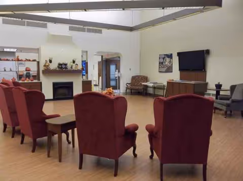 Senior living lounge with red chairs, tables, fireplace, and a wall-mounted TV.
