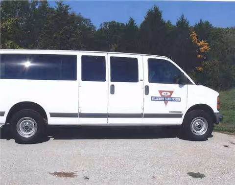 White Hillcrest Care Center van parked on a paved lot with trees in the background.